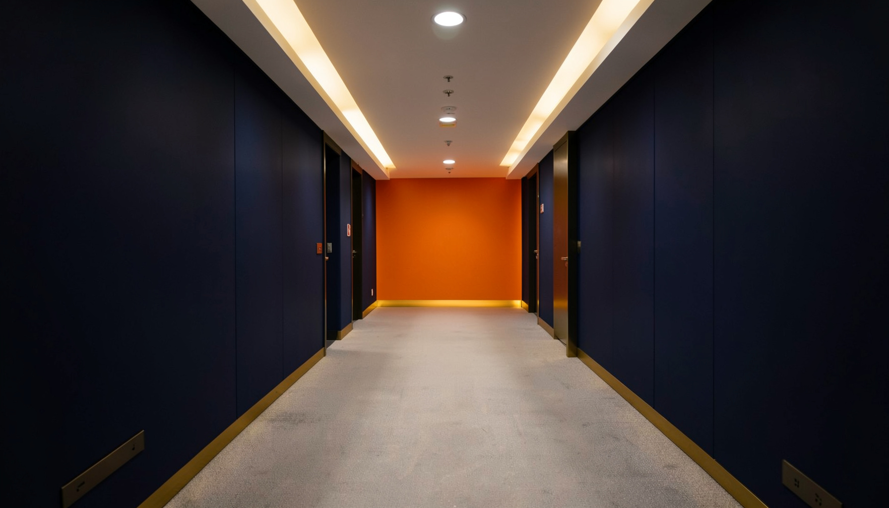 A quiet, softly lit conference hallway with deep navy walls and warm gold accent lighting, conveying a professional medical meeting atmosphere